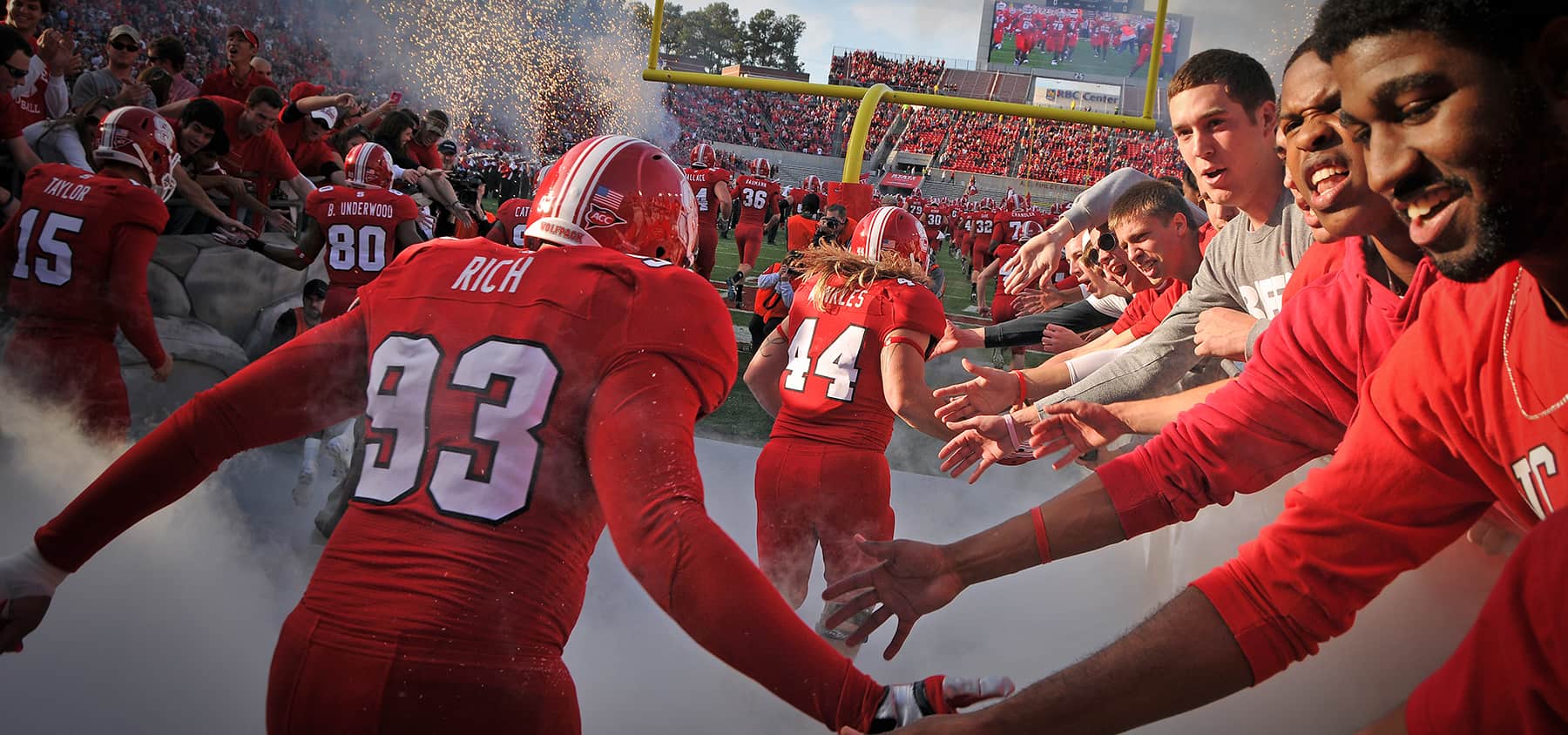 Players entering the field through a tunnel of fans, smoke, and fireworks
